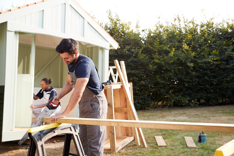 Charpentier masculin avec apprentie femme sciant du bois pour construire une tonnelle extérieure dans le jardin.