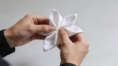 Mains pliant une serviette blanche en forme de fleur