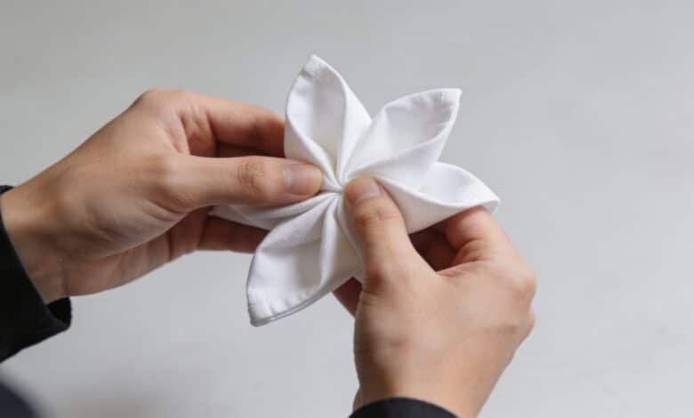 Mains pliant une serviette blanche en forme de fleur