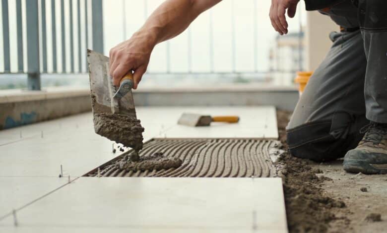 ouvrier agenouille versant mortier sur terrasse avant carrelage