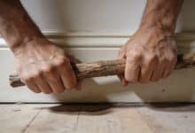 Mains serrant une baguette de bois contre plinthes.
