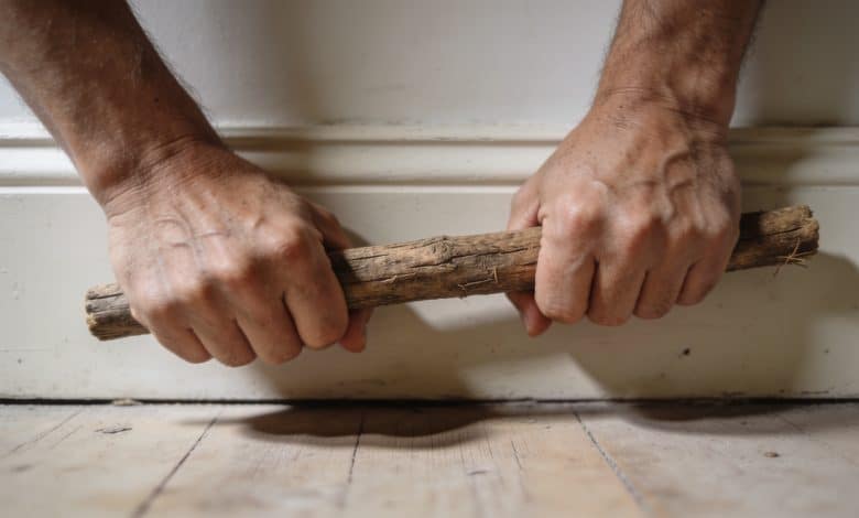 Mains serrant une baguette de bois contre plinthes.