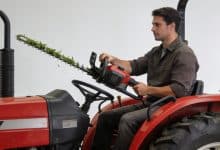 Operateur assis sur tracteur rouge maniant taille-haie allongee