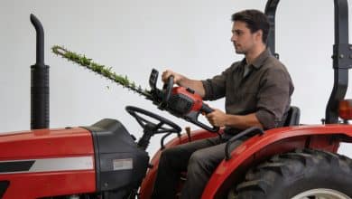 Operateur assis sur tracteur rouge maniant taille-haie allongee