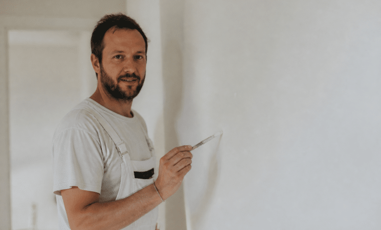 Peintre tenant un pinceau devant un mur blanc.