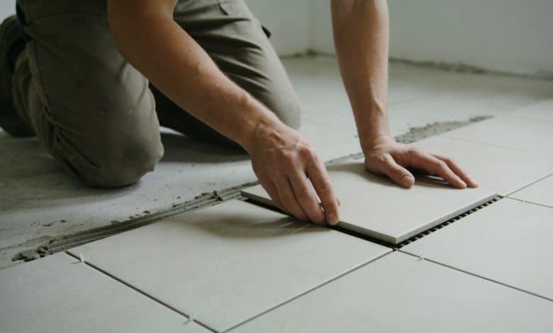 Personne agenouillée posant des carreaux au sol.