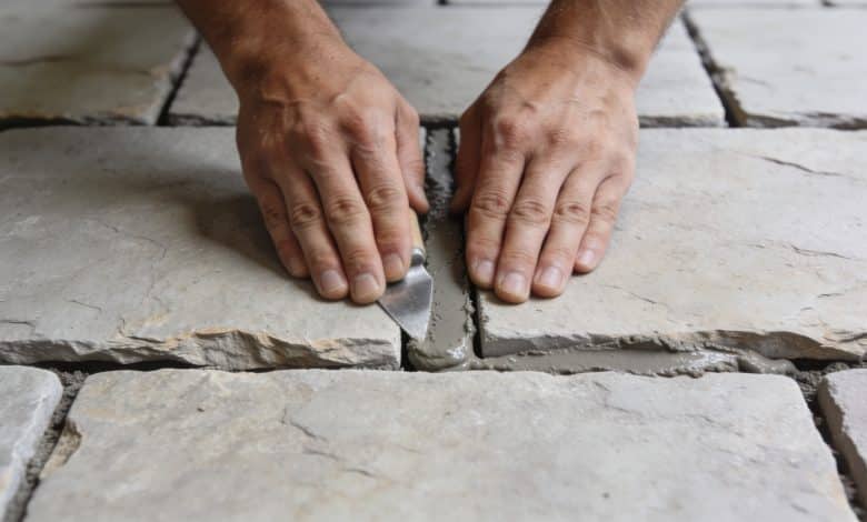 Mains appliquant du mortier entre carreaux de terrasse.