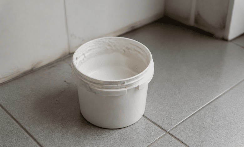 Pot de peinture blanche ouvert posé sur carrelage sanitaire