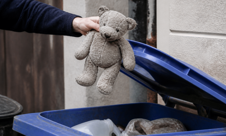 Main tenant peluche usee au-dessus bac recyclage ouvert